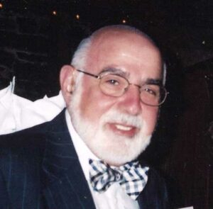 Man in navy pinstripe suit with glasses and white beard