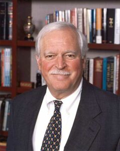 Man with white hair and mustache in navy suit and patterned tie