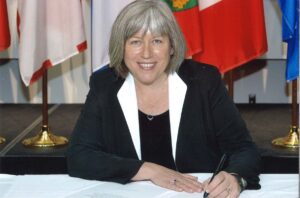 Woman sitting at table with grey hair and black jacket with white lapels